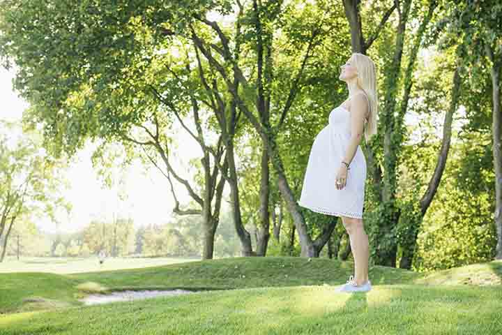 Pregnant smiling blond woman in white dress inhale fresh air in the park. Walk outdoor